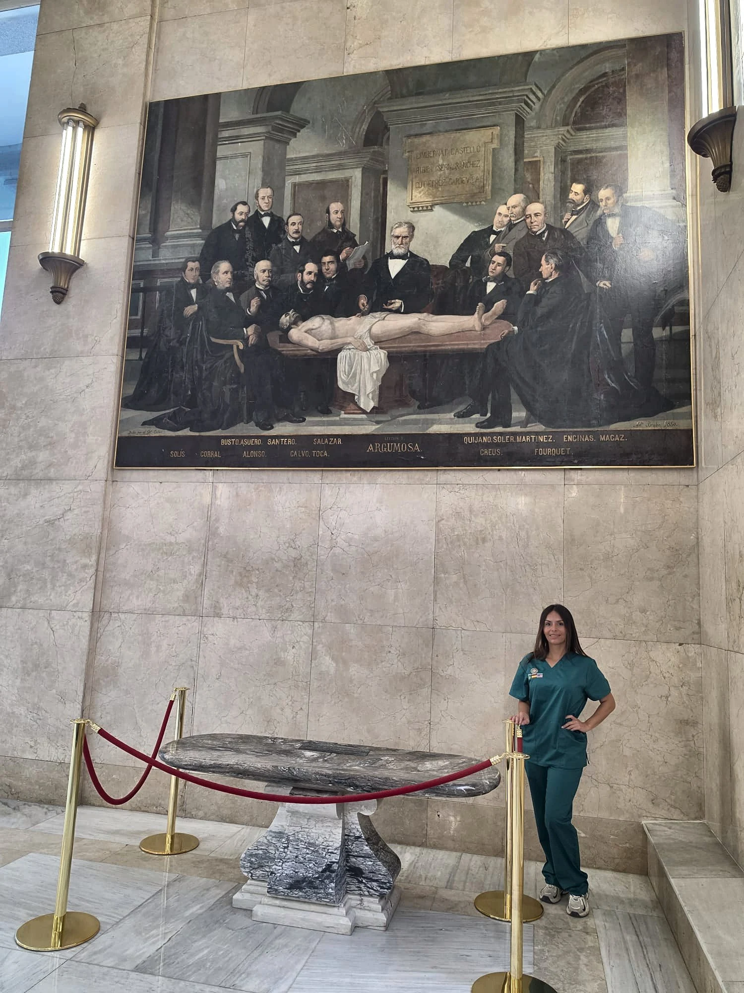 Cindy Alzate con pijama sanitario en el vestíbulo de la Facultad de Medicina, bajo el cuadro de la lección de anatomía del doctor Argumosa